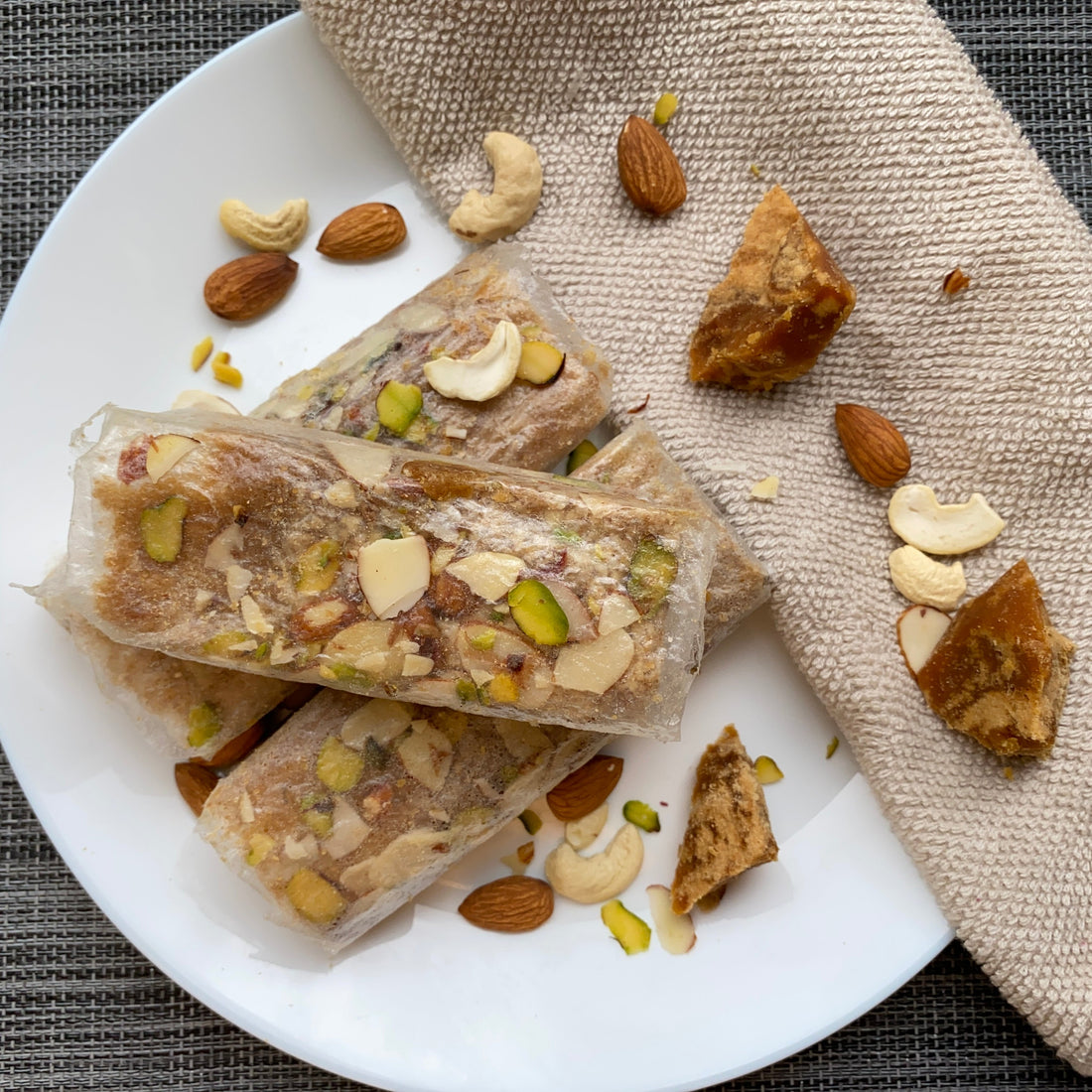 Dry fruit Pootharekulu placed on white plate sprinkled with almonds cashews and Jaggery block placed at the side