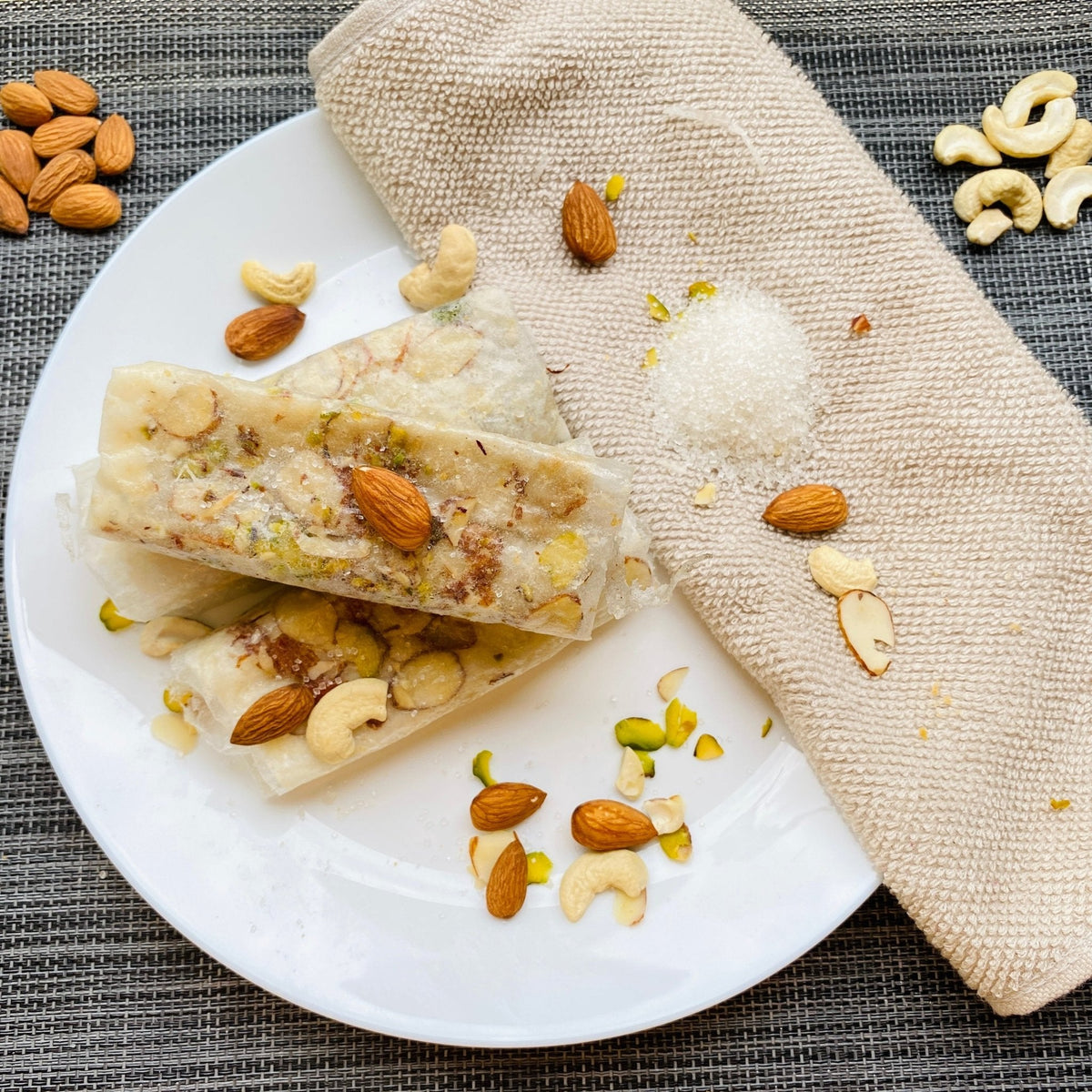 Close-up top view of Sugar Dry Fruit Cashew Almond Pistachio Papersweet rolls garnished with almonds, cashews and pistachios, with sugar and dry fruits scattered alongside