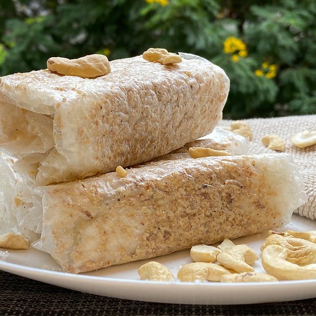 Close-up of Sugar Kaju Pootharekulu rolls topped with cashews, showing the thin layered paper sweet texture